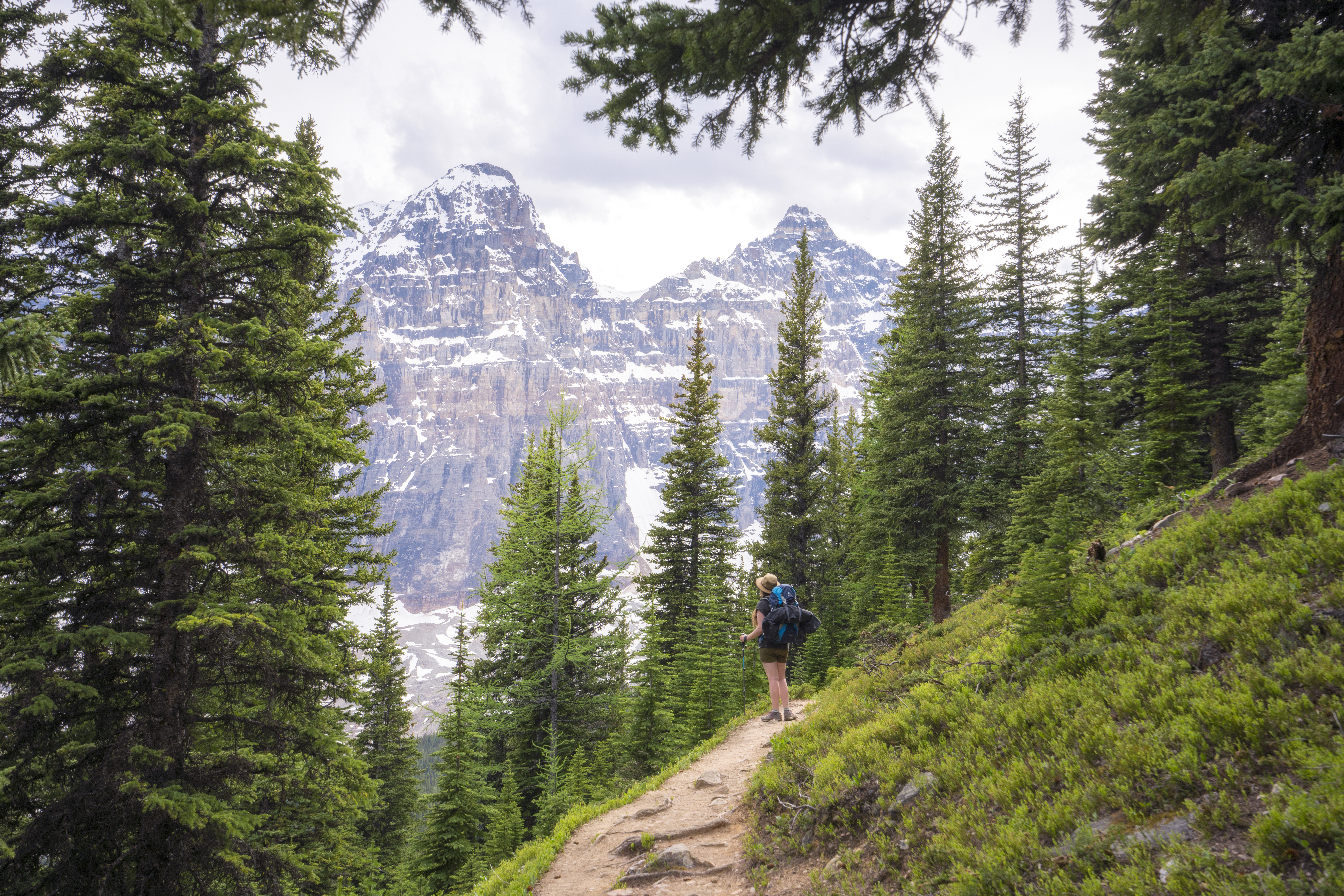 A hiker stops along a curved part of the Eiffel Lake Trail to look at the mountains
