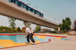 A person skateboarding in a colourful outdoor skatepark with train overhead