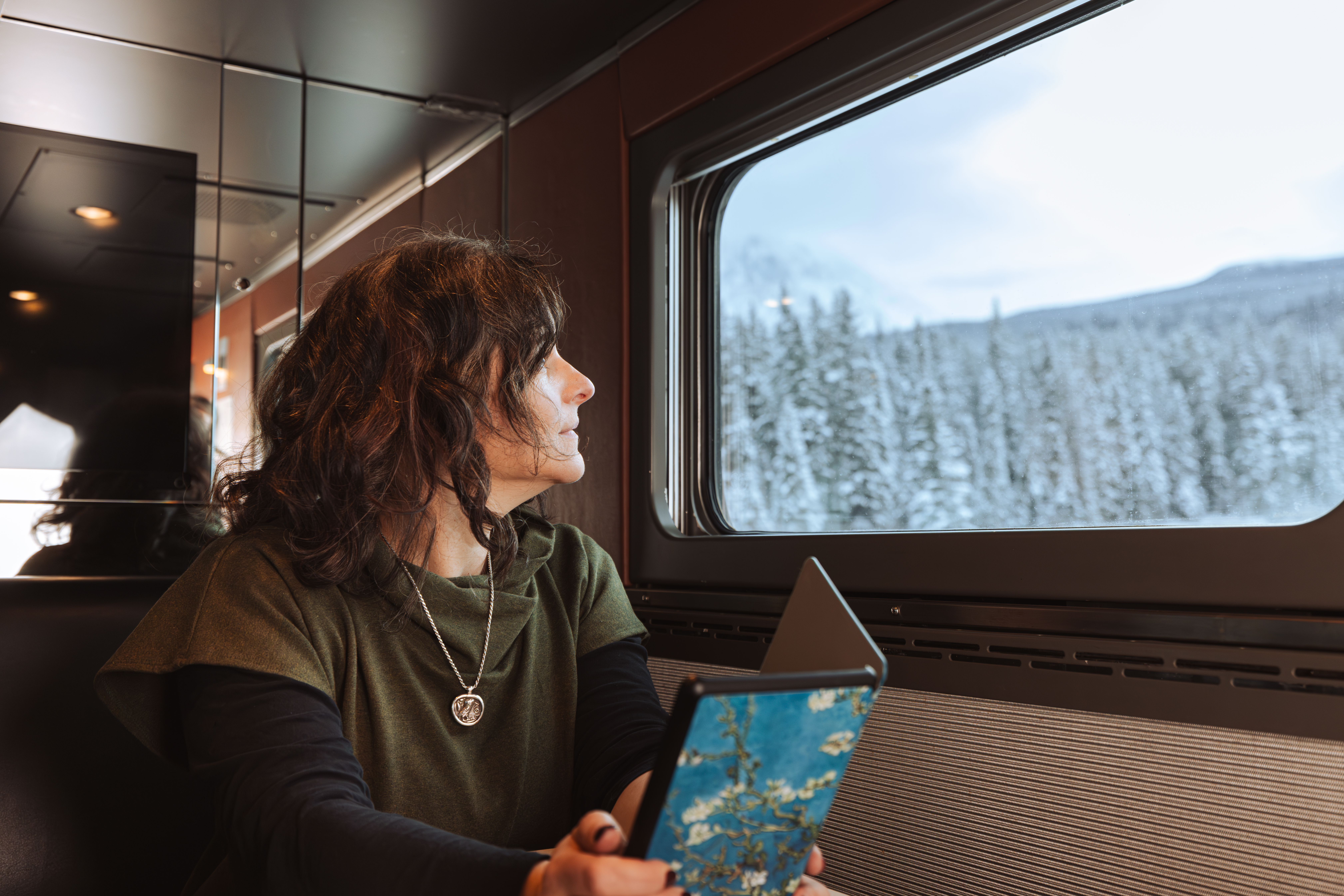 Seated mature woman onboard VIA Rail's train, The Canadian, looks out window at snowy landscape during winter