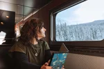 Seated mature woman onboard VIA Rail's train, The Canadian, looks out window at snowy landscape during winter