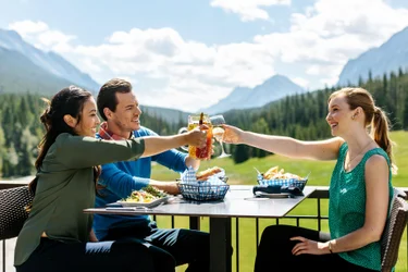 A trio of friends charge glasses over a meal on the outdoor patio at Banff Spring's Waldhaus bistro.