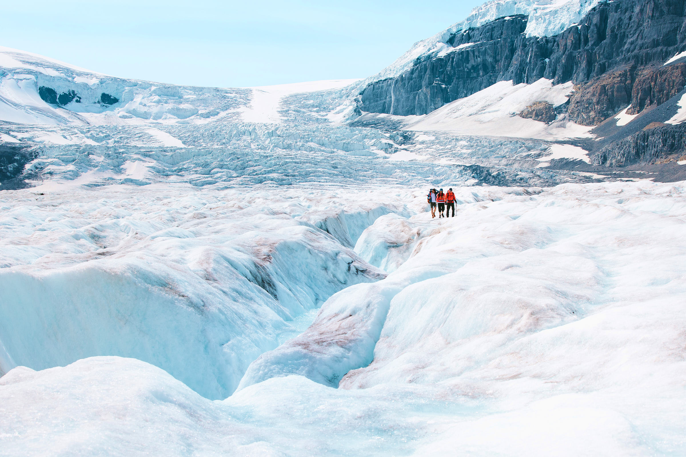 Three people walking on a large glacier 