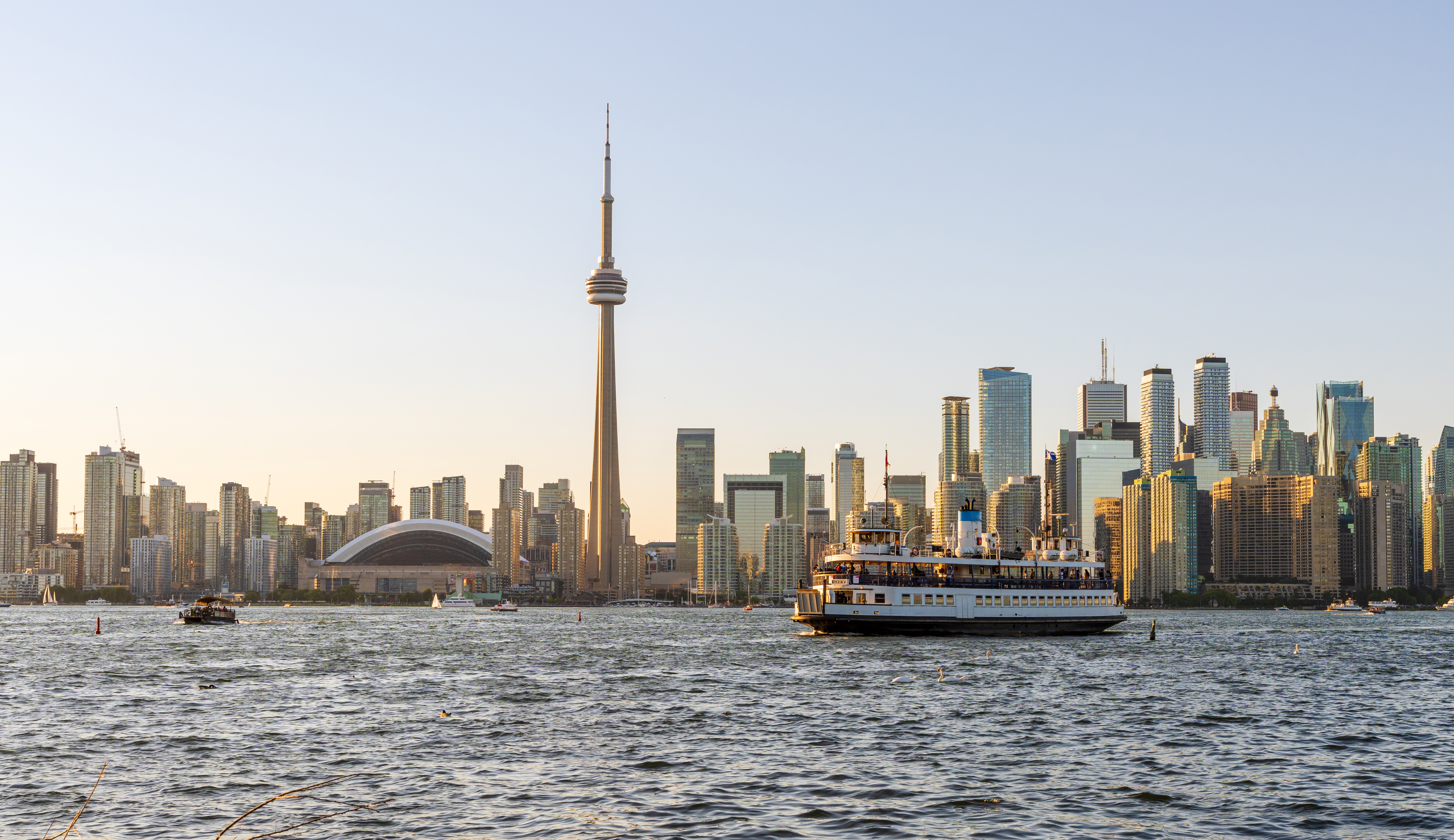View of Toronto Island Ferry passing by city skyline at sunset