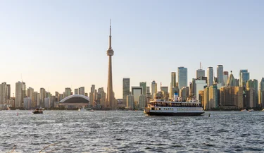 View of Toronto Island Ferry passing by city skyline at sunset