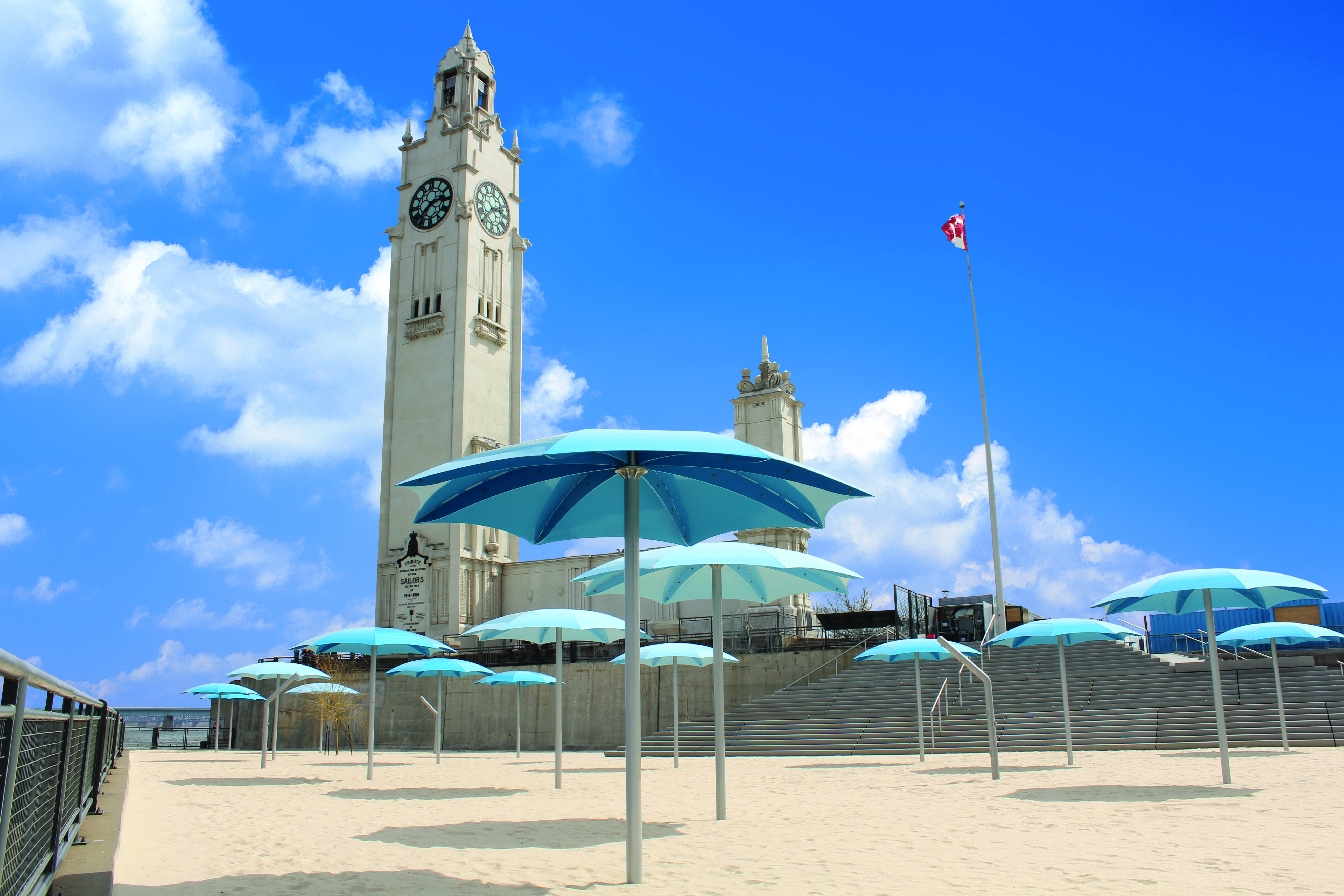 Sandy beach with blue umbrellas and tall clock tower behind 