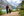 A couple holds hands and walks along a lakeside trail with mountains behind
