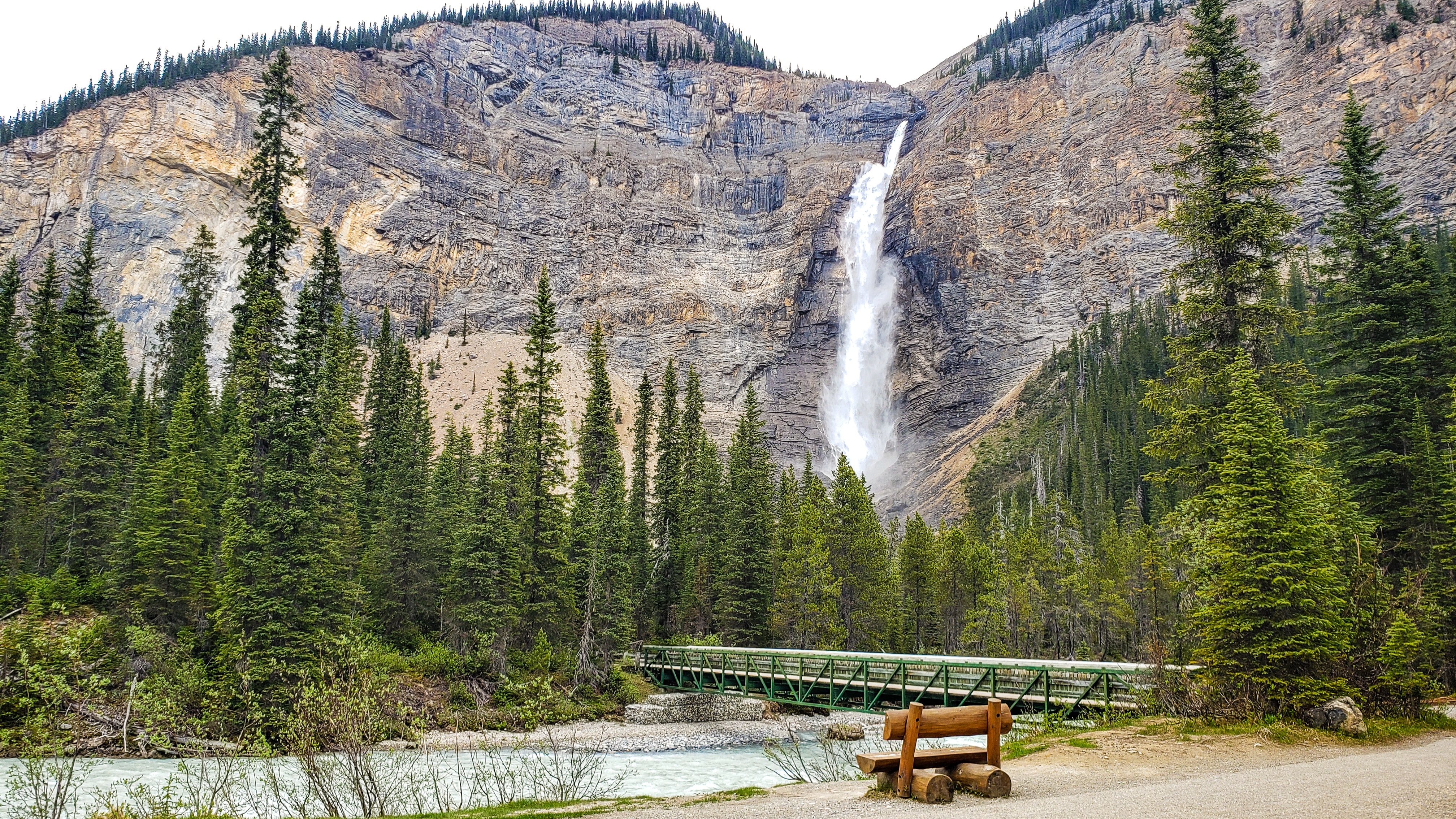A wooden bench in front of Takakkaw Falls, a tall waterfall