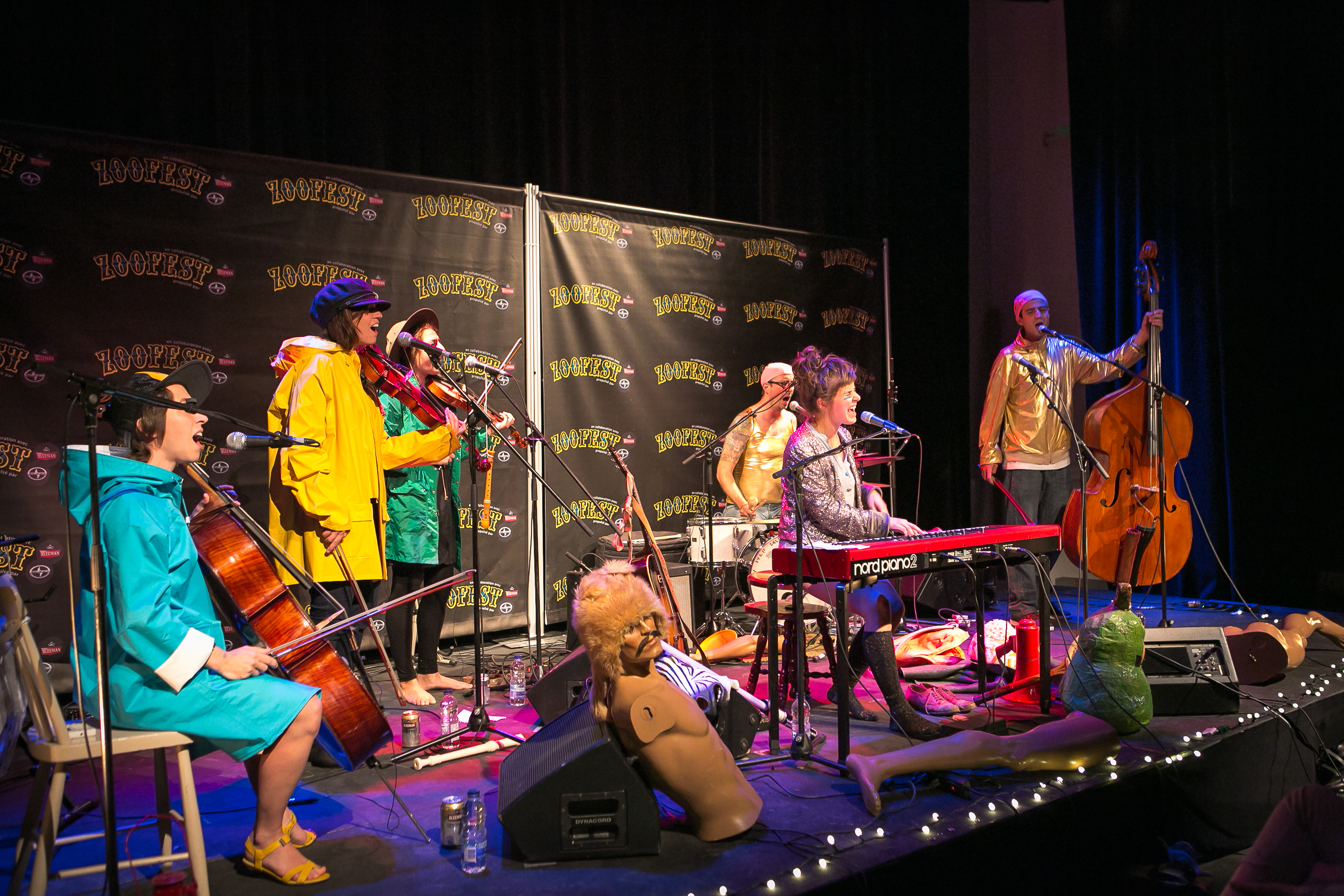 Comedians and musicians in raincoats and shiny jackets perform on stage at Zoofest