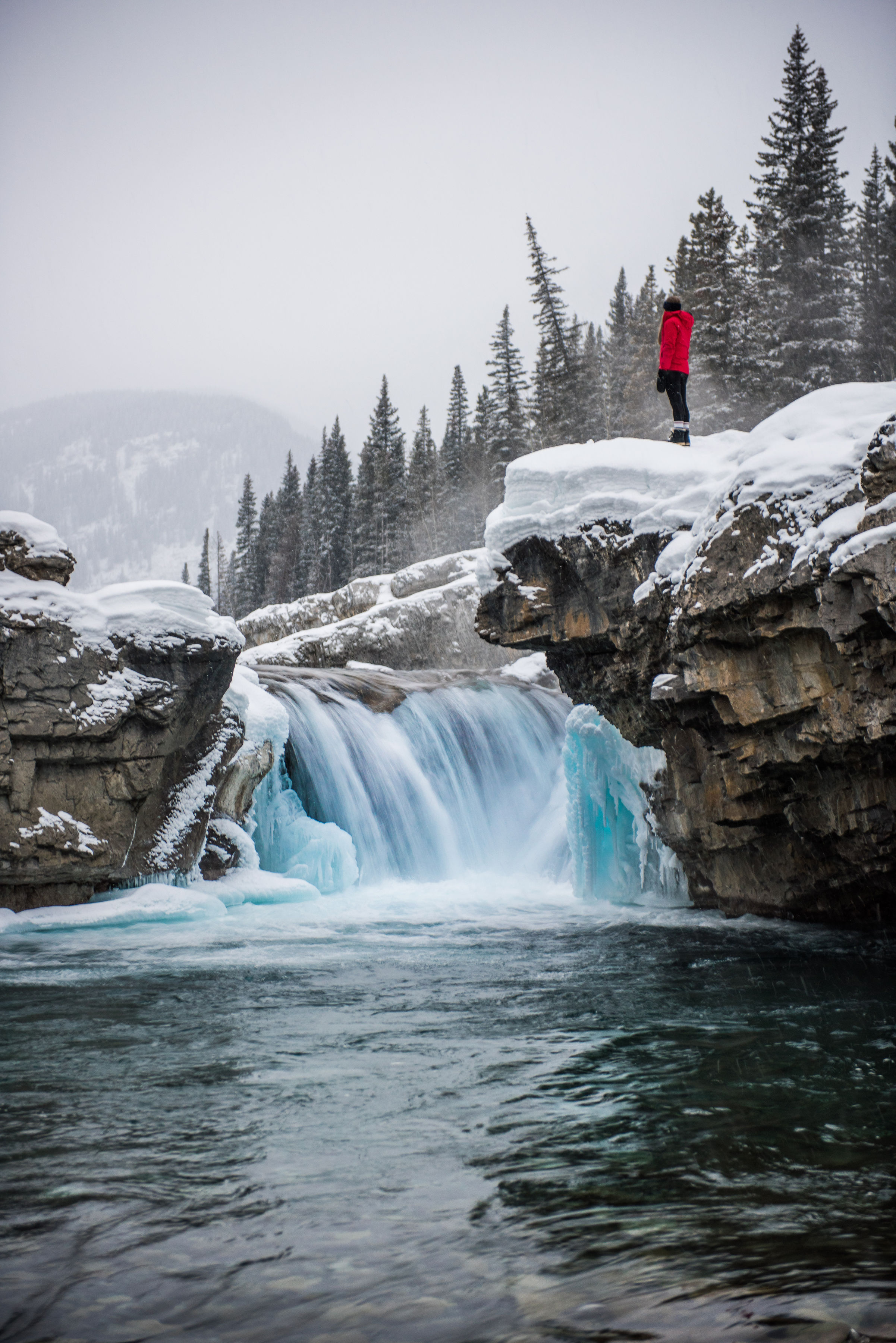 Water tumbles down nearly frozen waterfall lined with huge rocks covered in white layers of snow in the Rocky Mountains