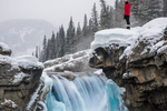 Water tumbles down nearly frozen waterfall lined with huge rocks covered in white layers of snow in the Rocky Mountains