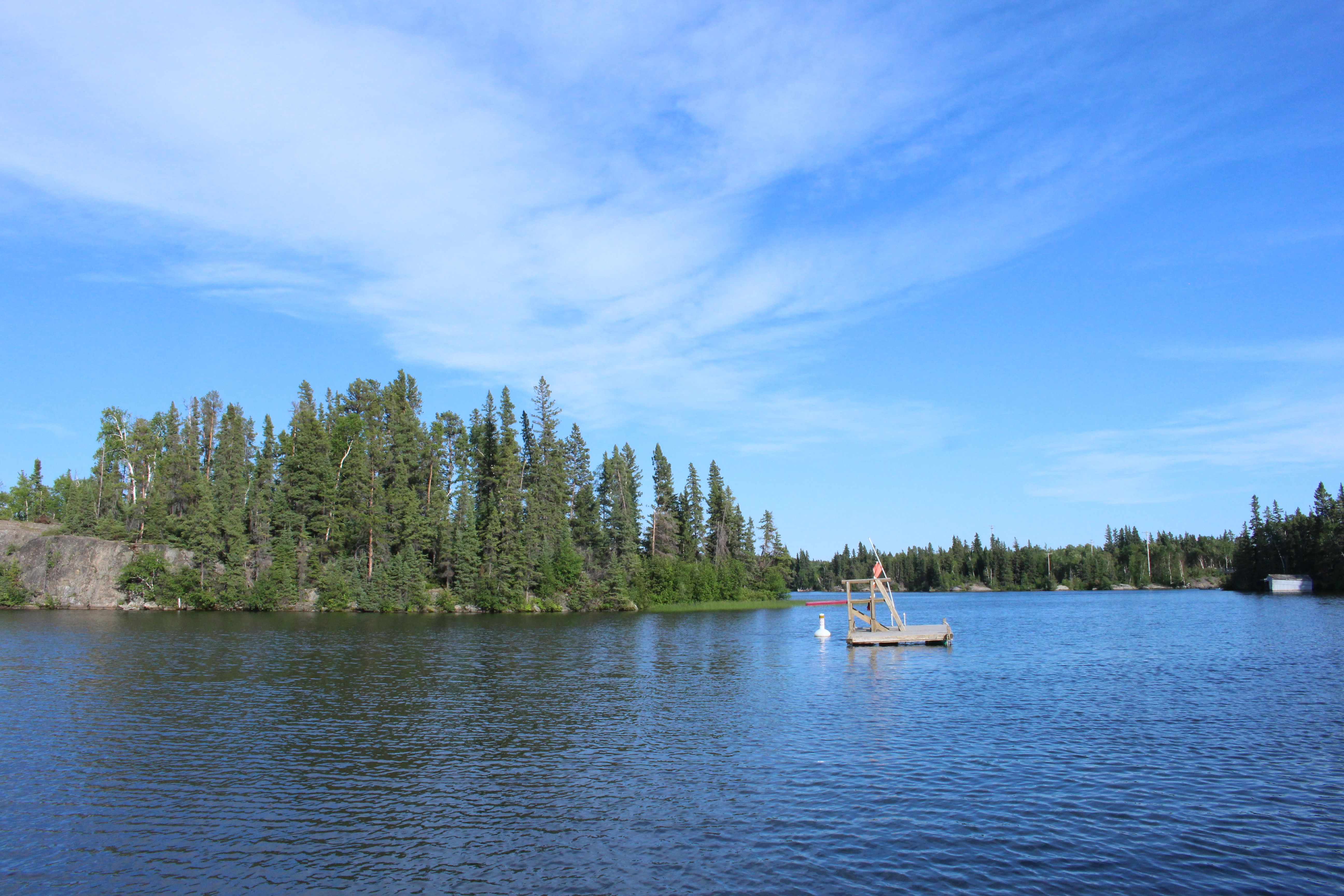 A small wooden dock floating in the middle of a lake with forest behind