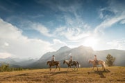 Three cowboys/cowgirls lead horses through mountains, Alberta