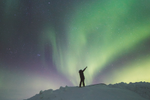 A person standing on snowy ground beneath pristine colourful Northern Lights with their arms reaching upwards and in the air 