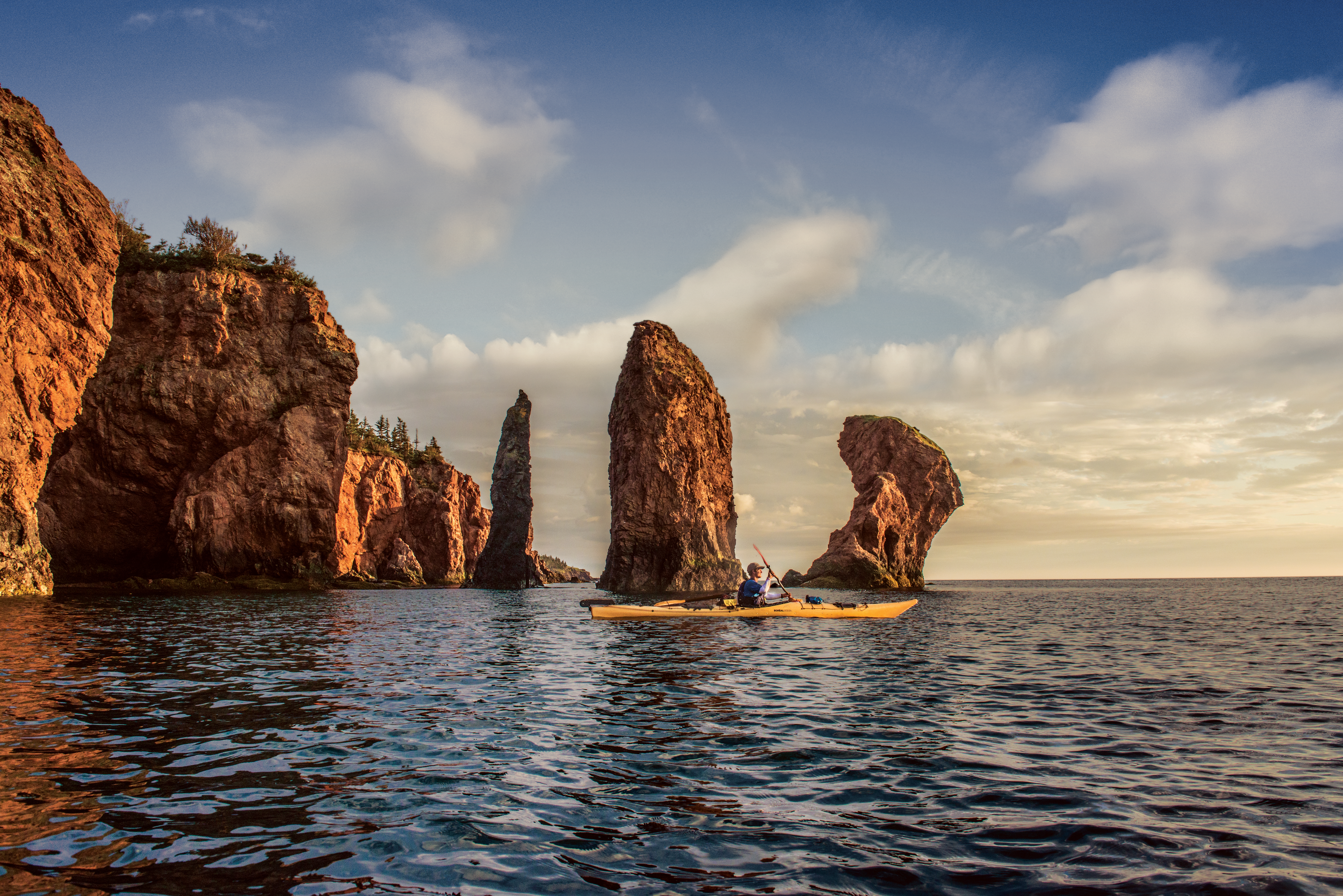 Kayaker near clay coloured and dramatic Three Sisters sea stacks in Cape Chignecto