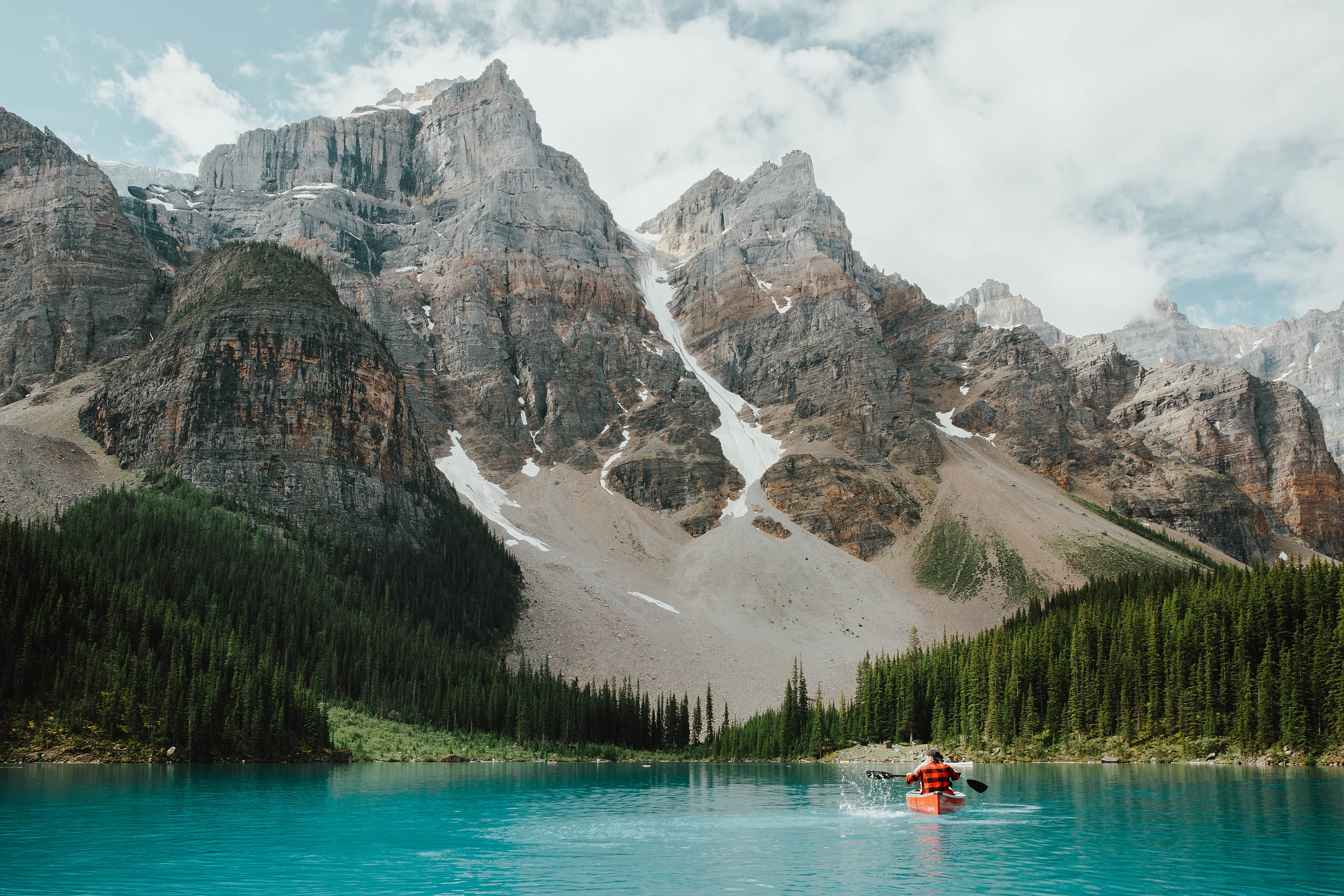 A person canoes on Moraine Lake with mountains in front of them