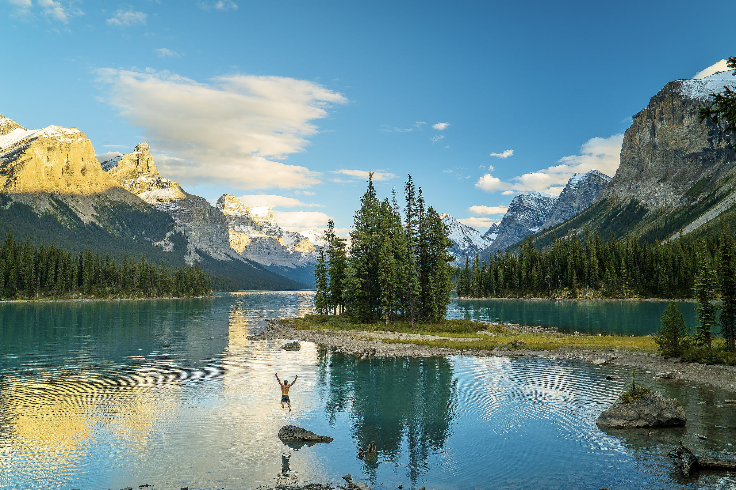 A person jumps into a turquoise lake in front of mountains