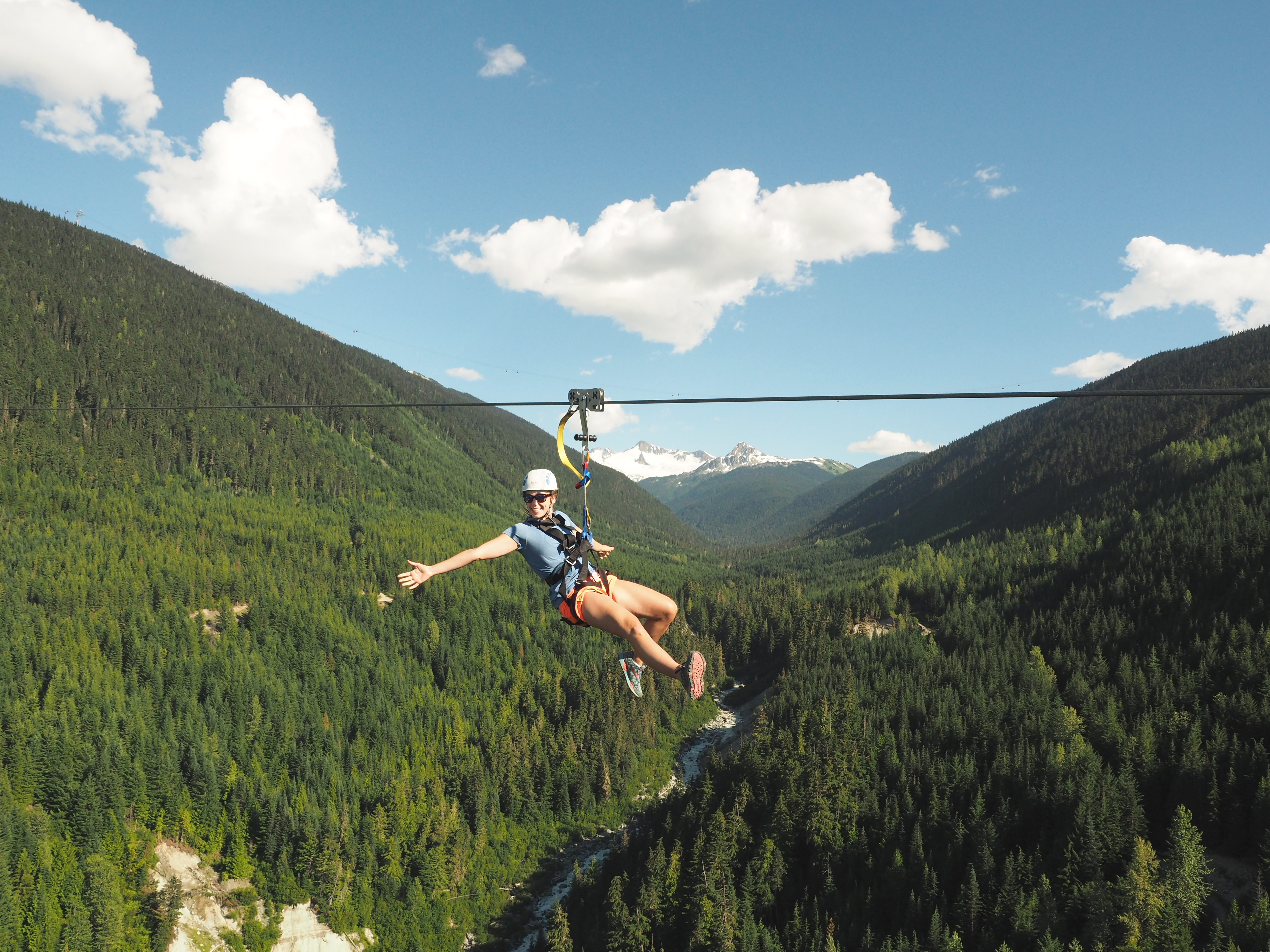 Person on a zipline hanging above the trees and river in Whistler