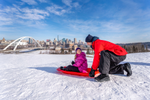 A dad helping a child on a toboggan with view of Edmonton city in the distance