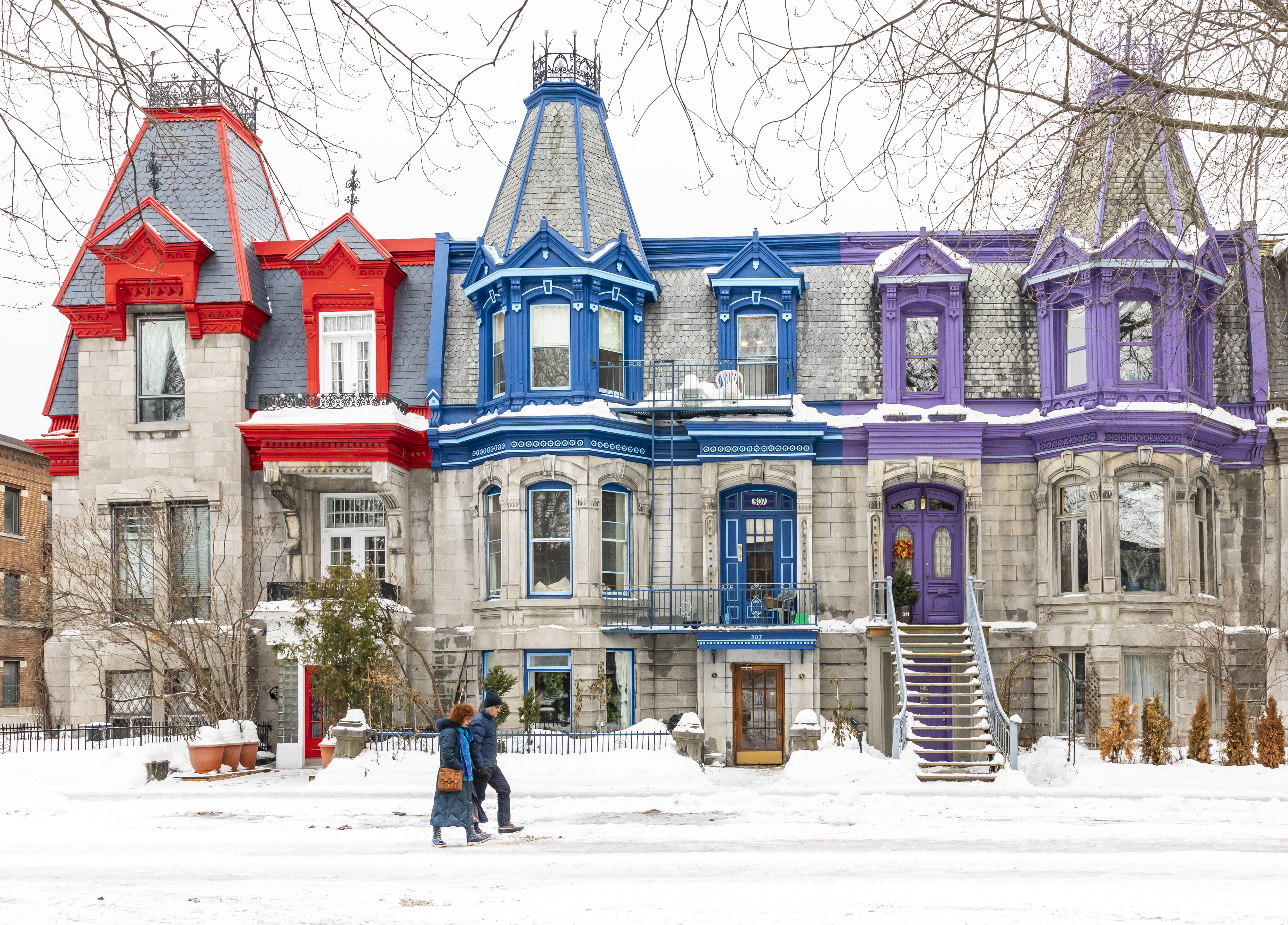 A couple walk through snowy Square Saint Louis, past colourful Victorian row houses