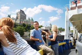 A young man leans against the side of a ferry as it cruises past the Fairmont Chateau Frontenac in Quebec City.