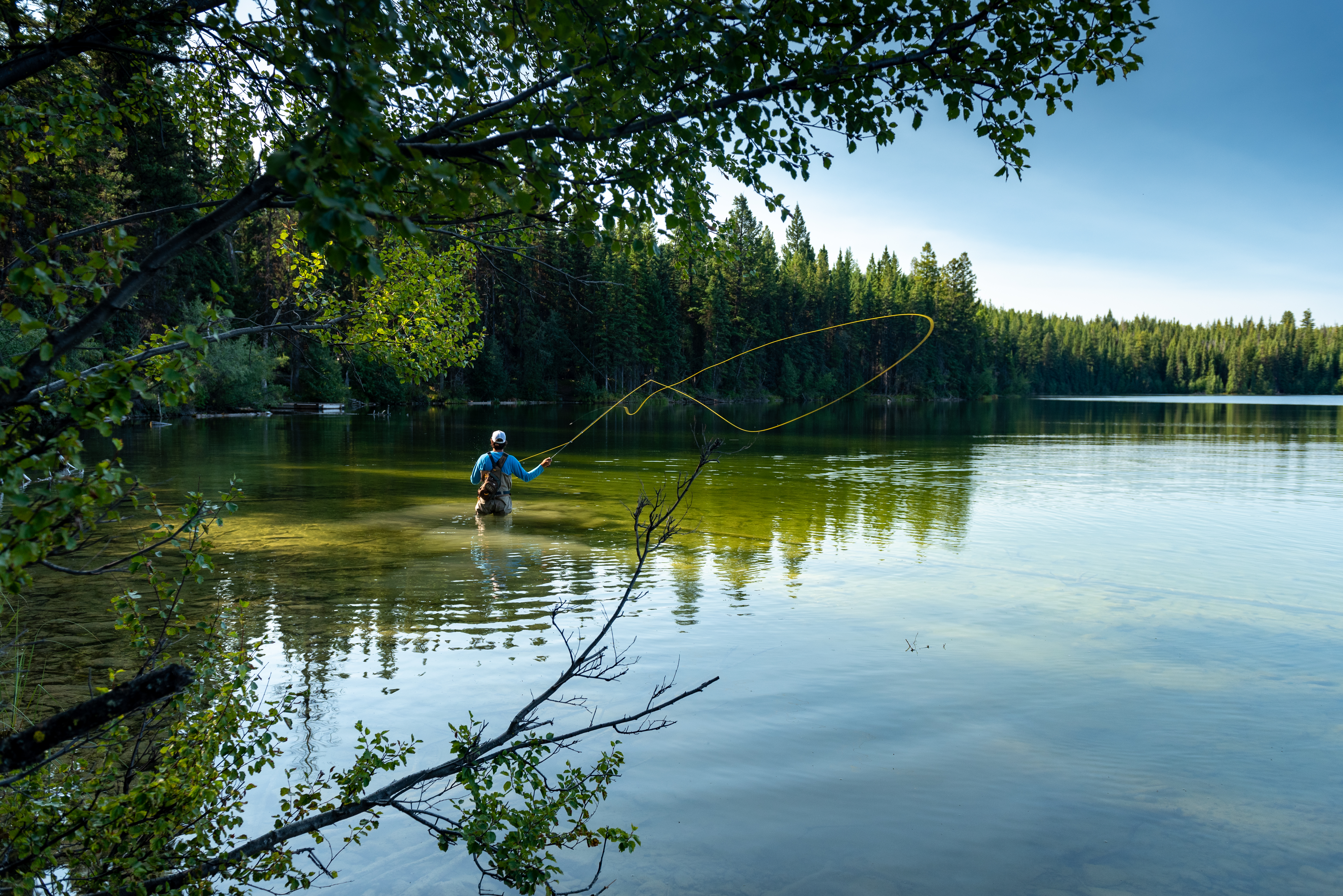 A person stands in a lake and casts his fishing rod 