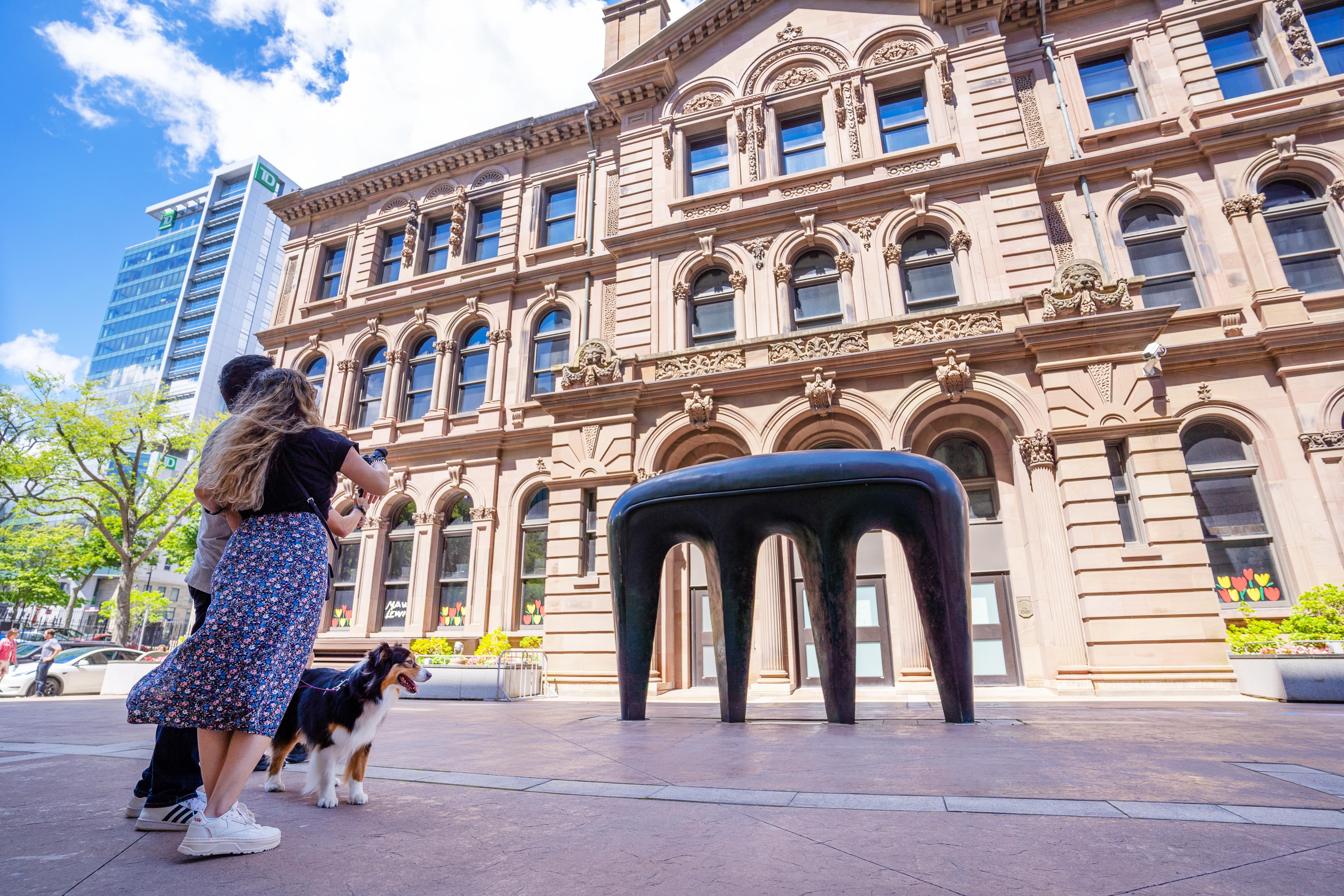 A couple and their dog take a photo of a sculpture outside the Art Gallery of Nova Scotia