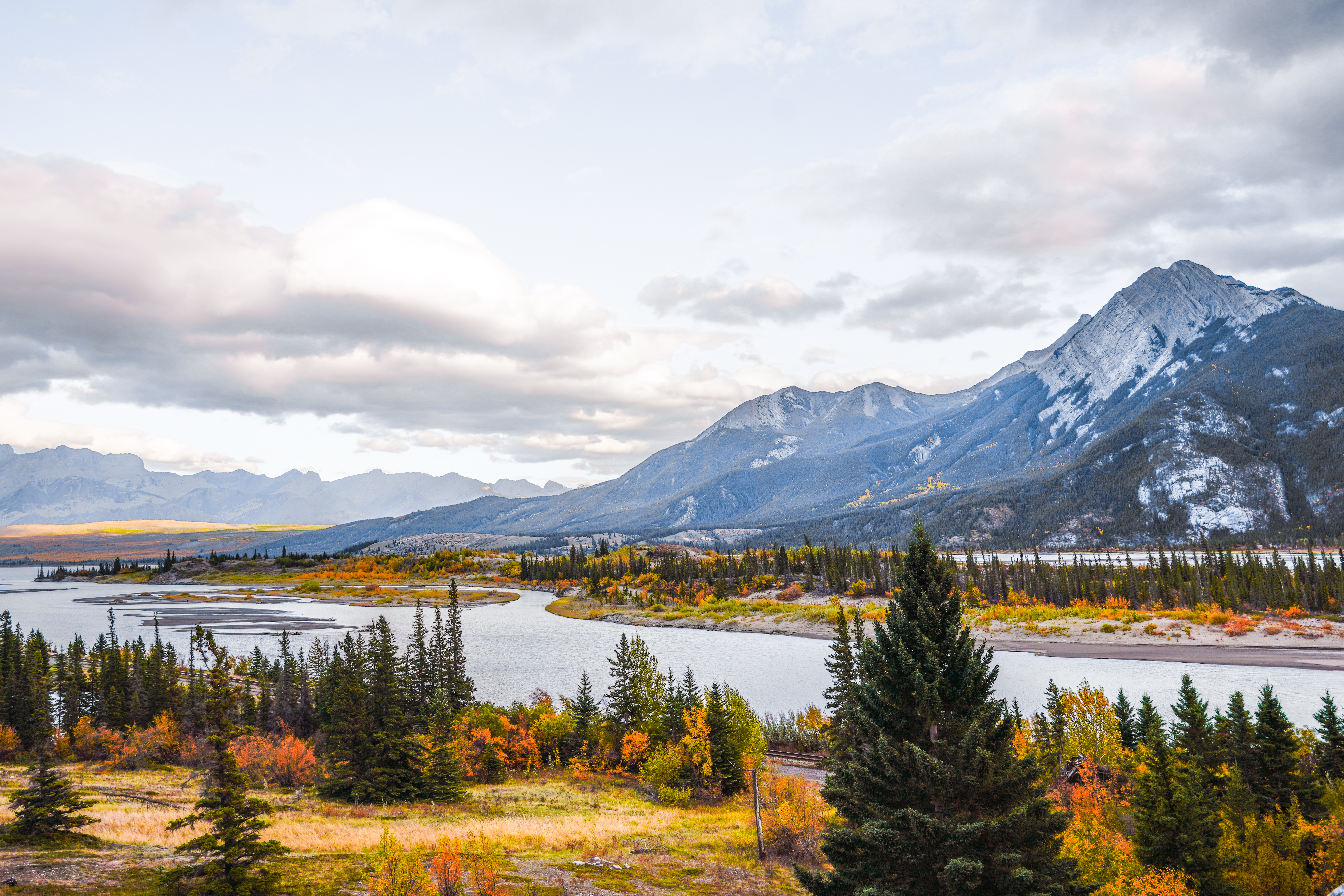  Fall colours by the river, towering mountains, and cloudy sky