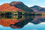 In the Laurentian Mountains, hills with orange and red maple trees are reflected in a lake 