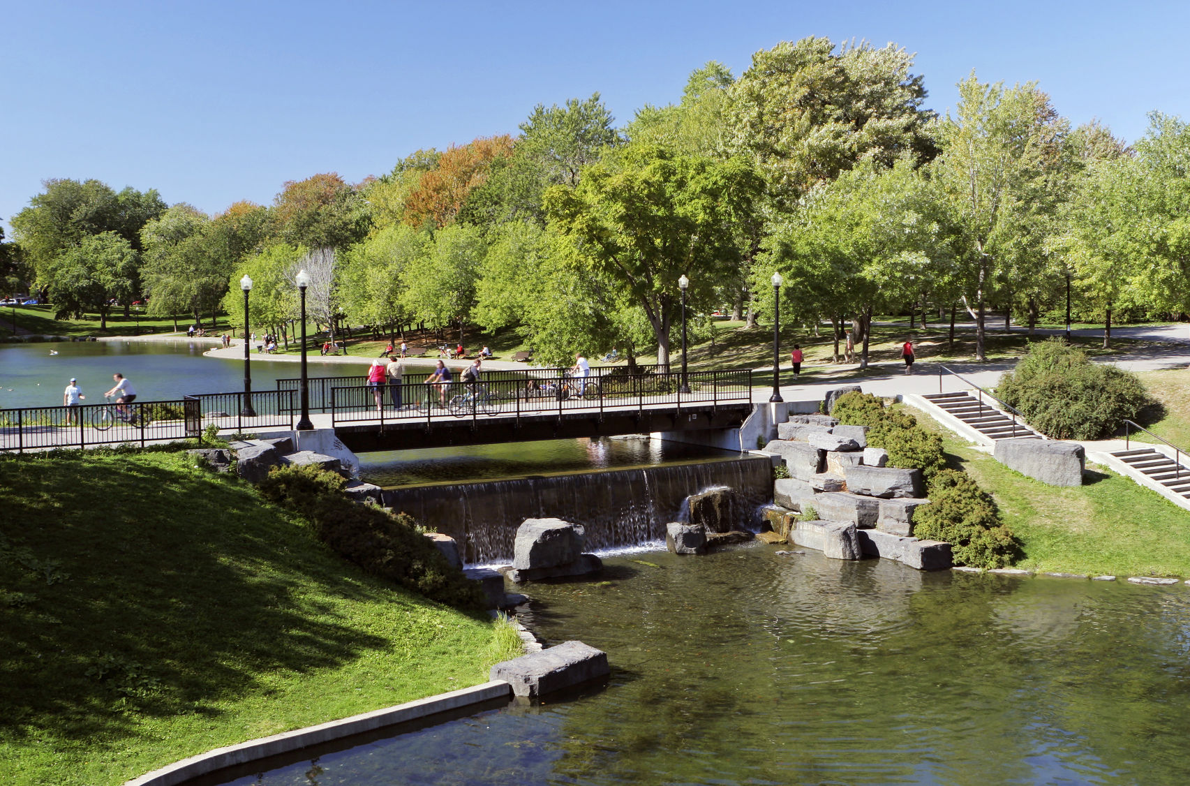 Cyclists riding over a bridge in an urban park on a sunny day in Fontaine Park