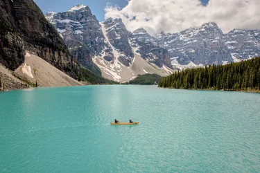 People paddling a yellow canoe surrounded by mountains at Moraine Lake in Banff National Park