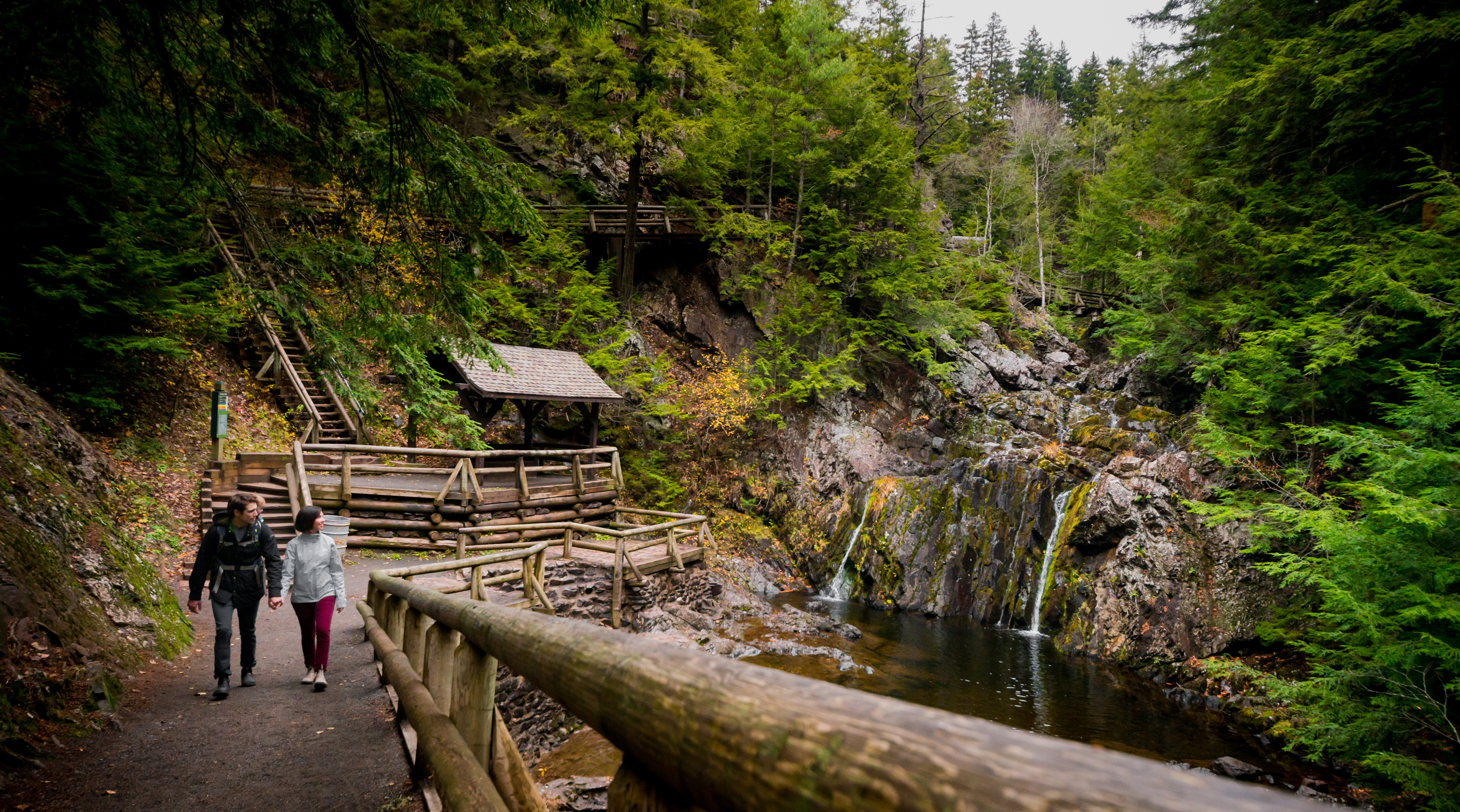 A couple walks along a trail past a waterfall in Victoria Park