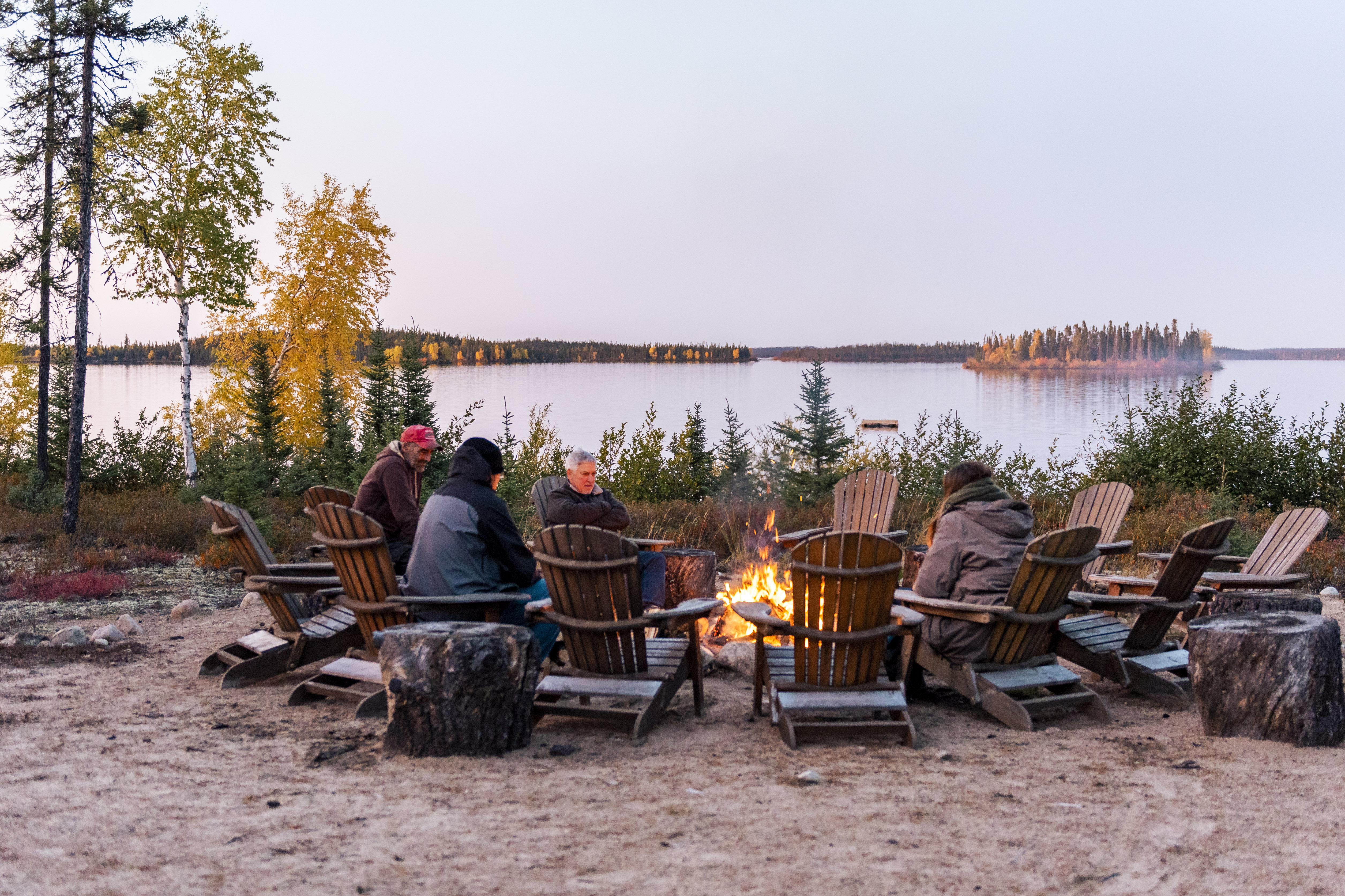 A group of people are sitting around a campfire on the waters edge