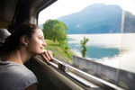 A woman leans against a train window and looks out at a lake