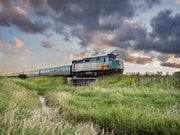 A VIA Rail Train rolls through a grassy field at sunset
