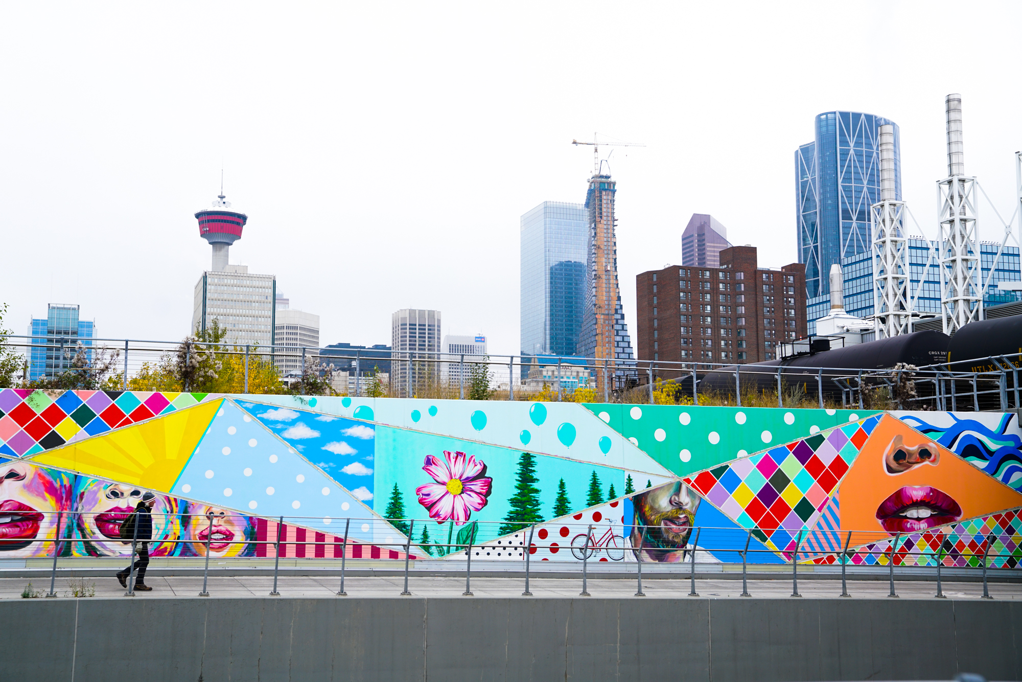 Person walking past a long colourful art mural in Calgary’s East Village