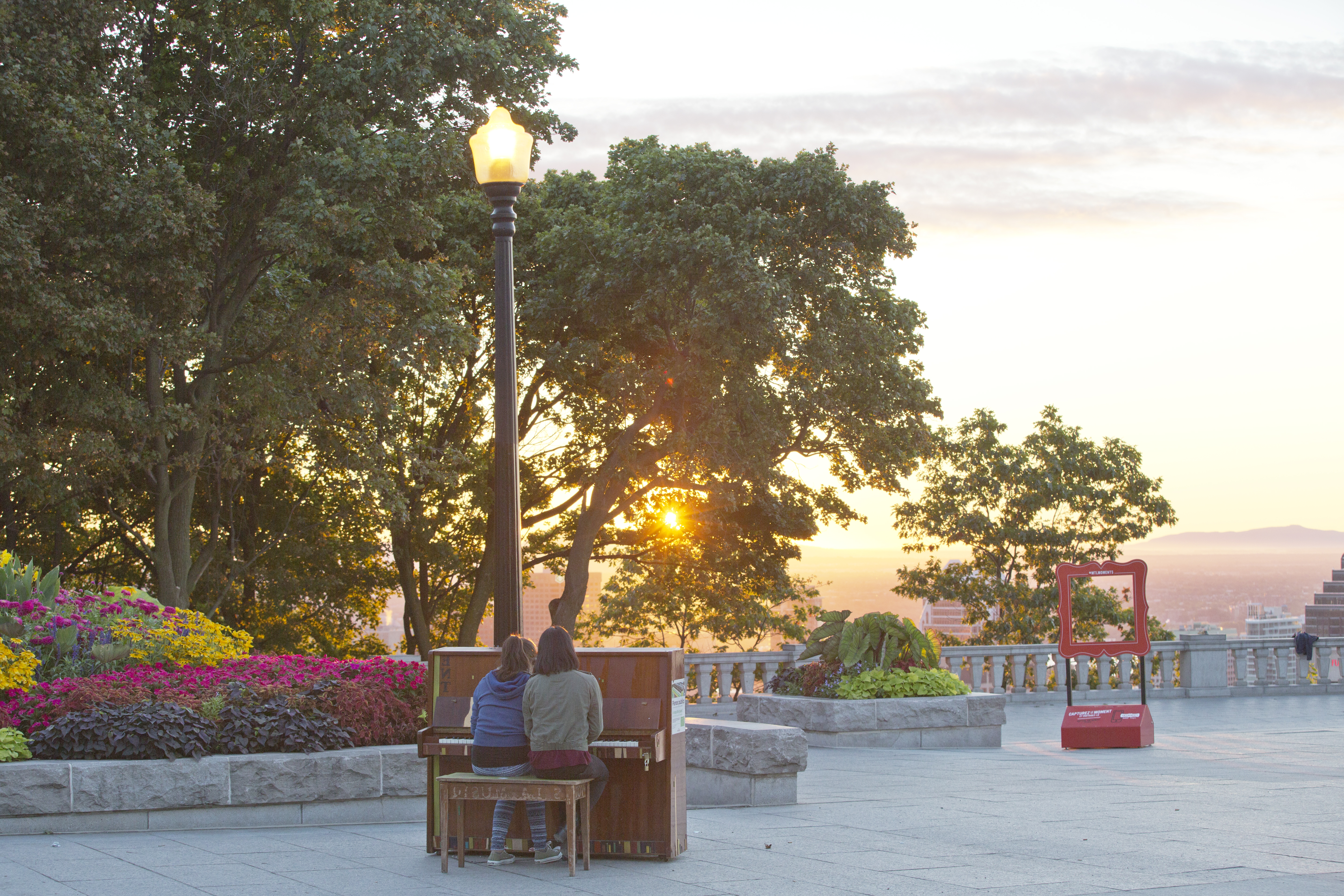 People playing on a free piano at the top of Mount Royal Park as the sun sets