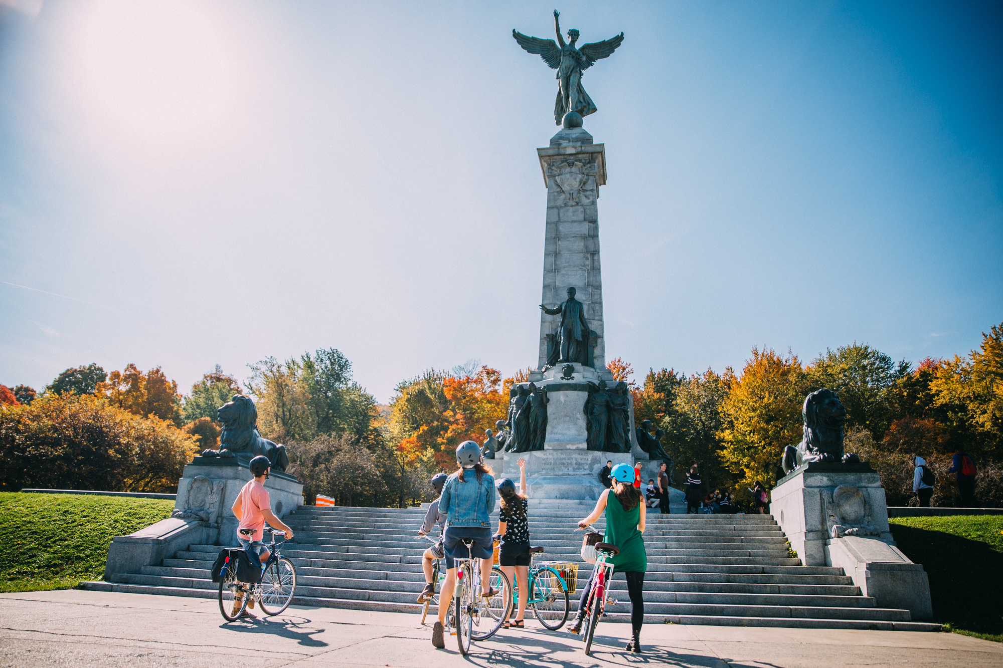 A group of cyclists stop to look at the Sir George-Étienne Cartier Monument with fall colours behind