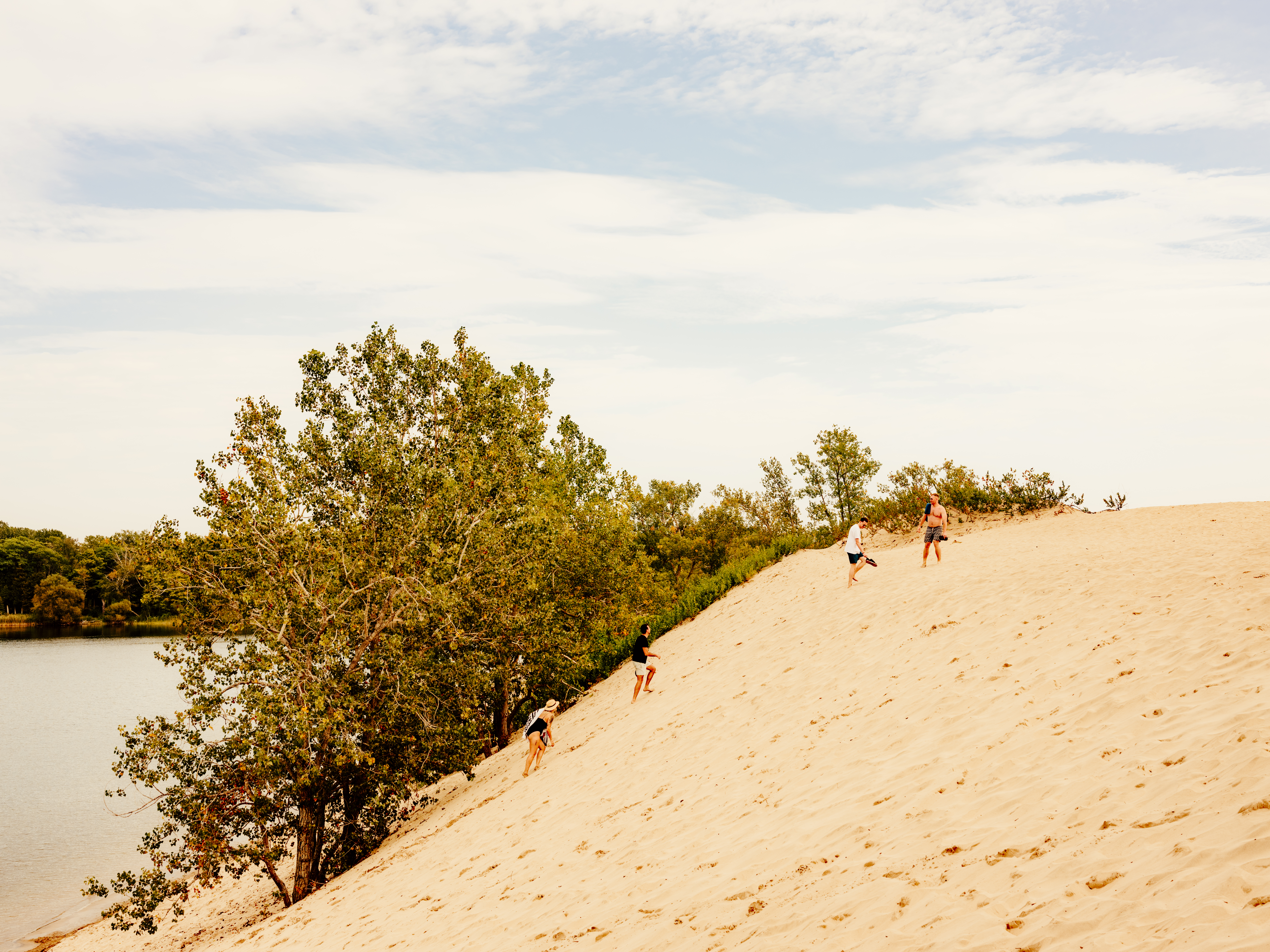 A group of friends climbing up a sand dune near a lake