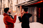 Couple smile and pose with maple sap lollipops outside of sugar shack, La Sucrerie de la Montagne, surrounded by maple trees after snow