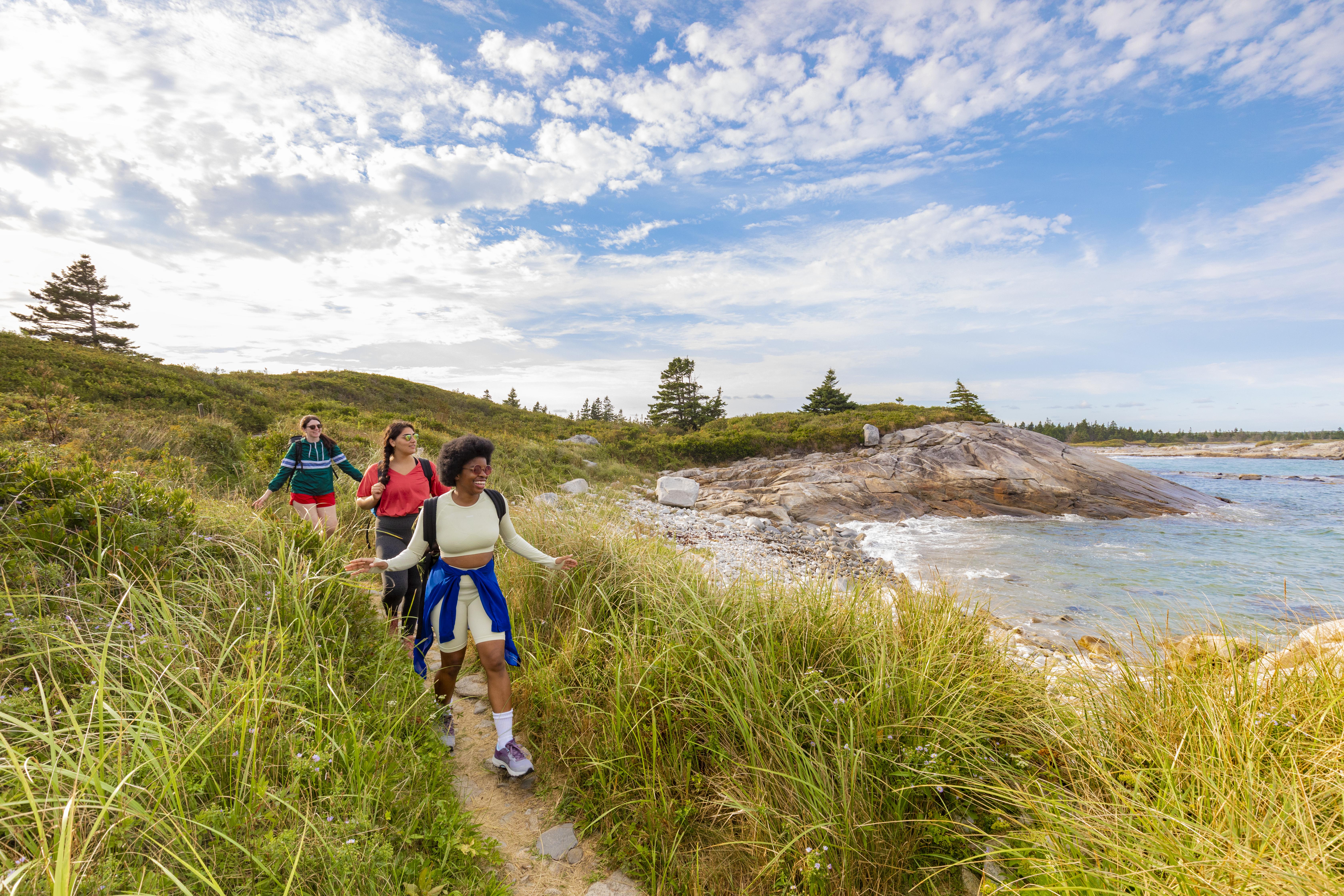 Three people walking gleefully on a trail by Keji Seaside's shore in Kejimkujik National Park