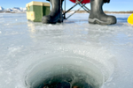 Person wearing boots sits with line in the water while ice fishing during the day in Canada 