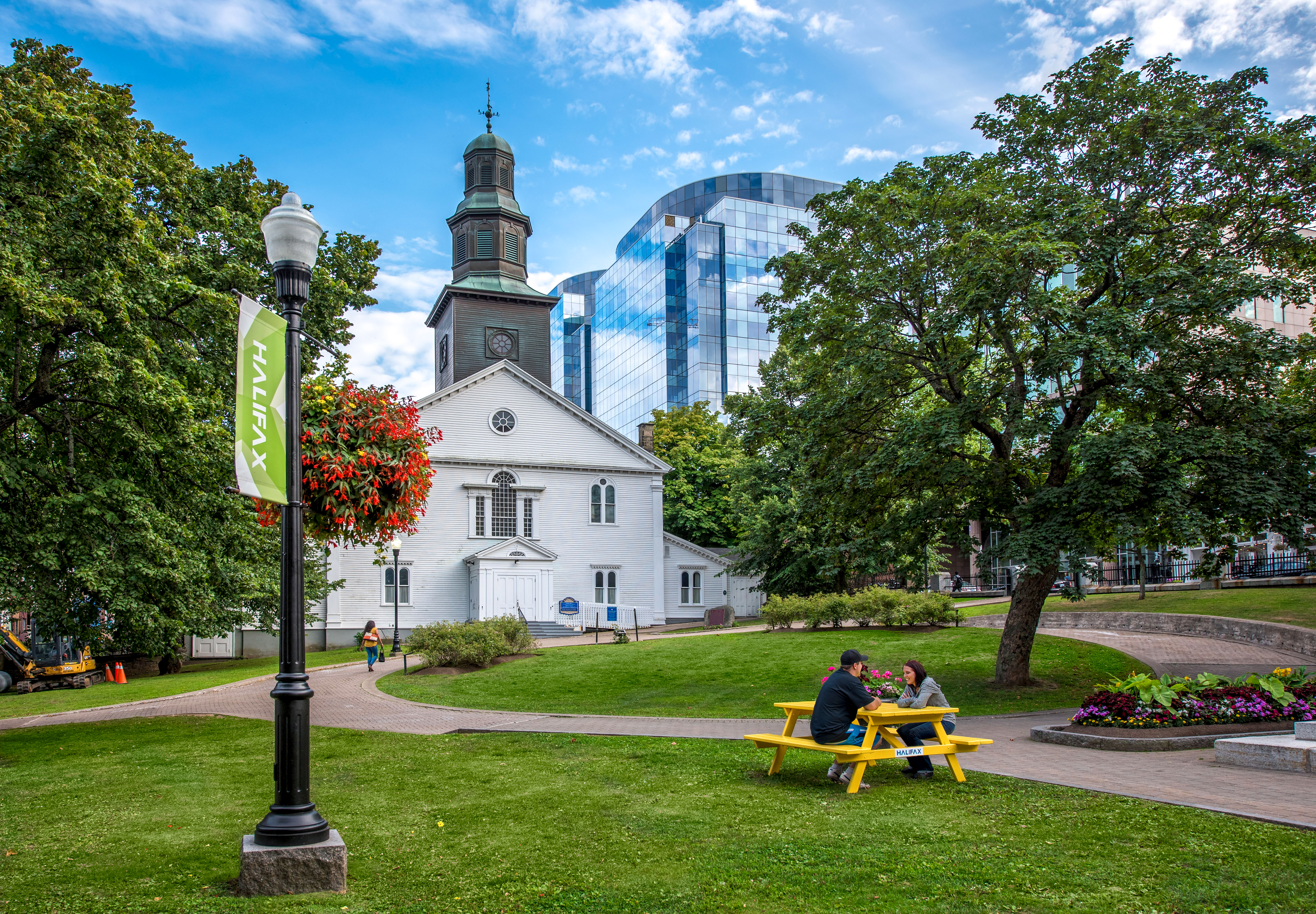 People sitting on a yellow picnic bench in a green space outside a church
