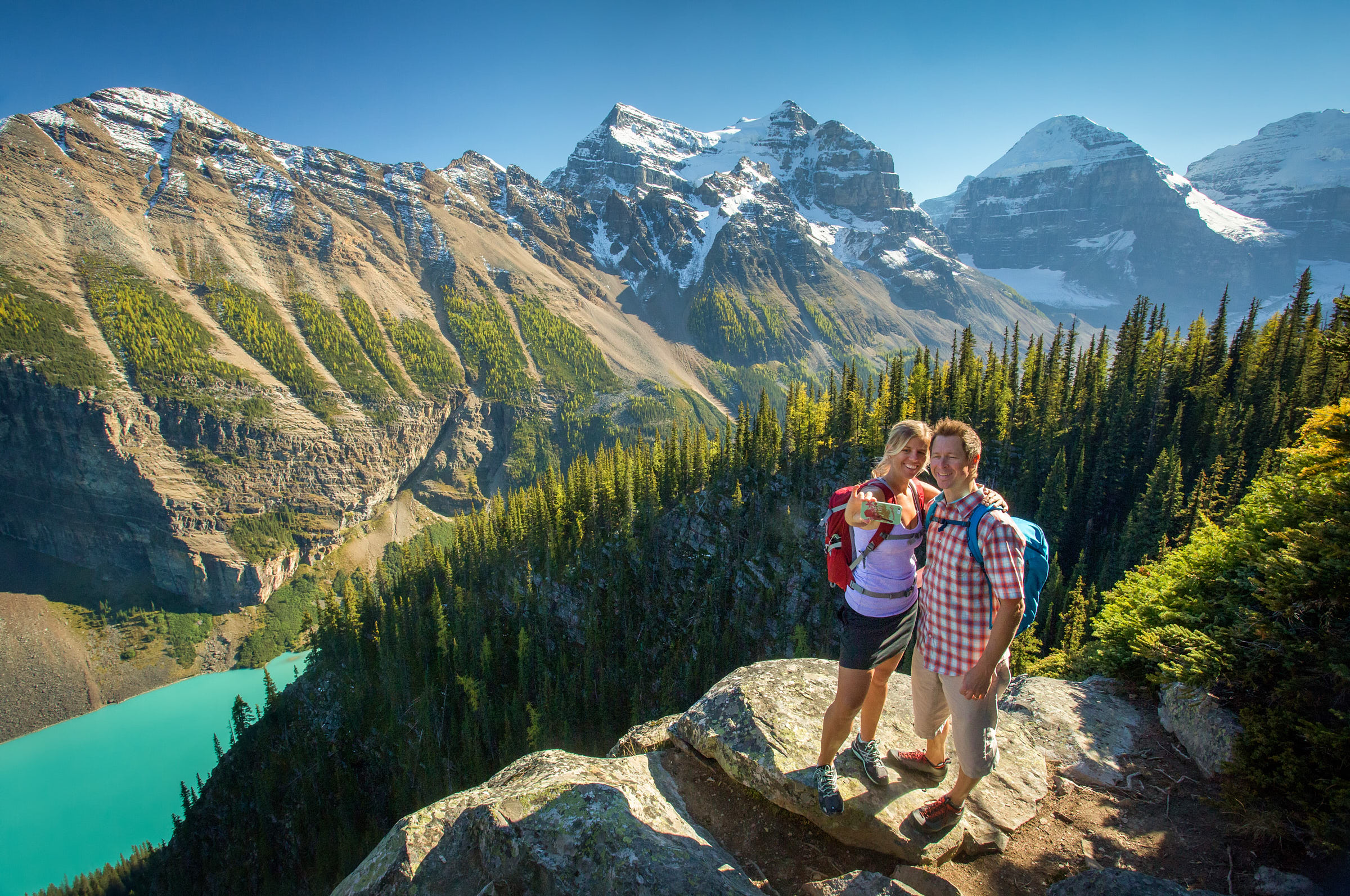 A couple capture a photo of themselves enjoying the view of mountains and lush forestry 