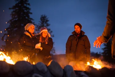 three people enjoying a large campfire outside