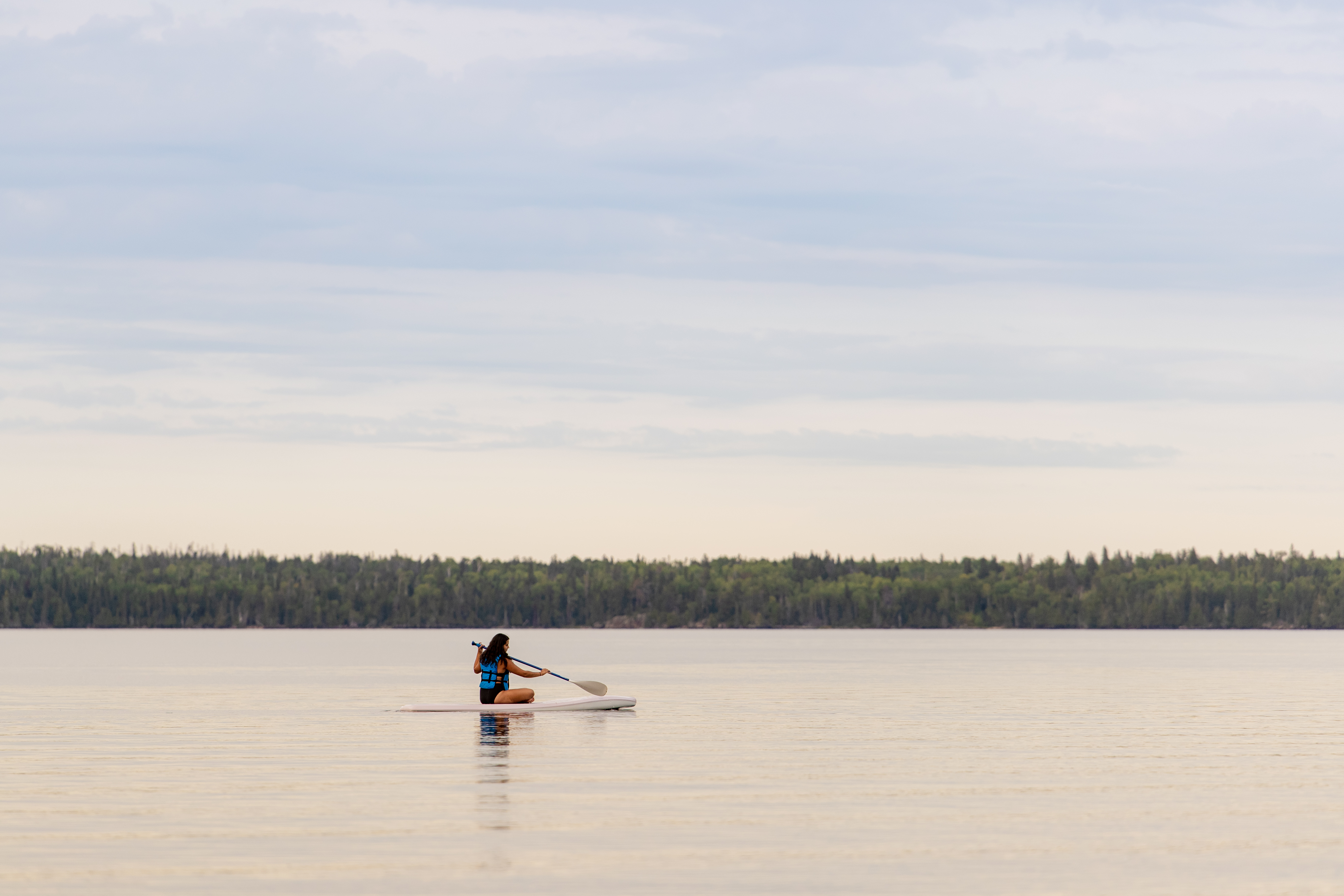 A girl sitting on a paddleboard on the calm water of West Hawk Lake