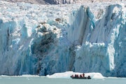 A zodiac boat sails underneath a tall calving glacier in a Bay in Alaska
