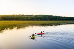 Two kayakers on paddling on a calm lake as the sun sets