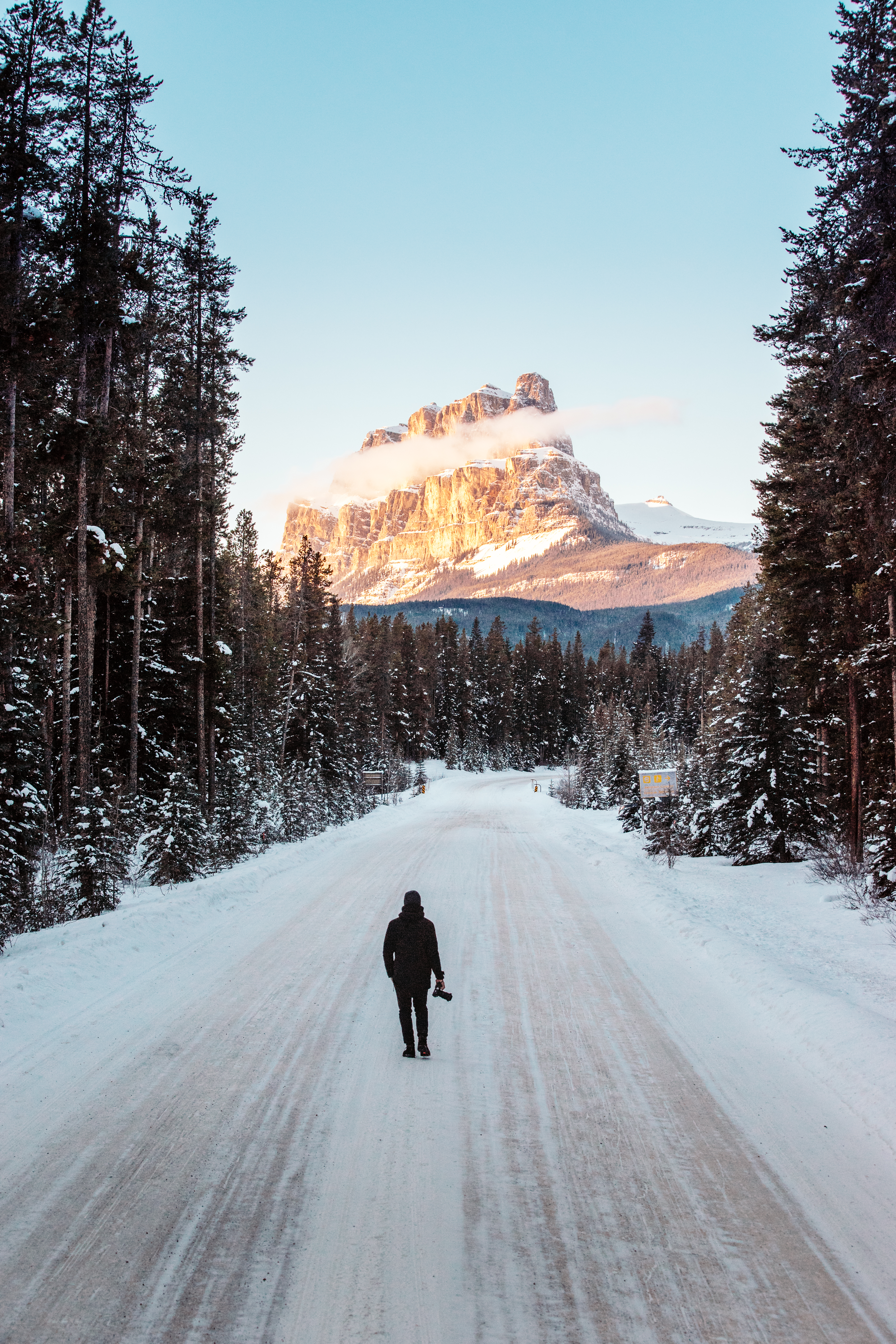 Man standing on the snowy Bow Valley Parkway looking at Castle Mountain
