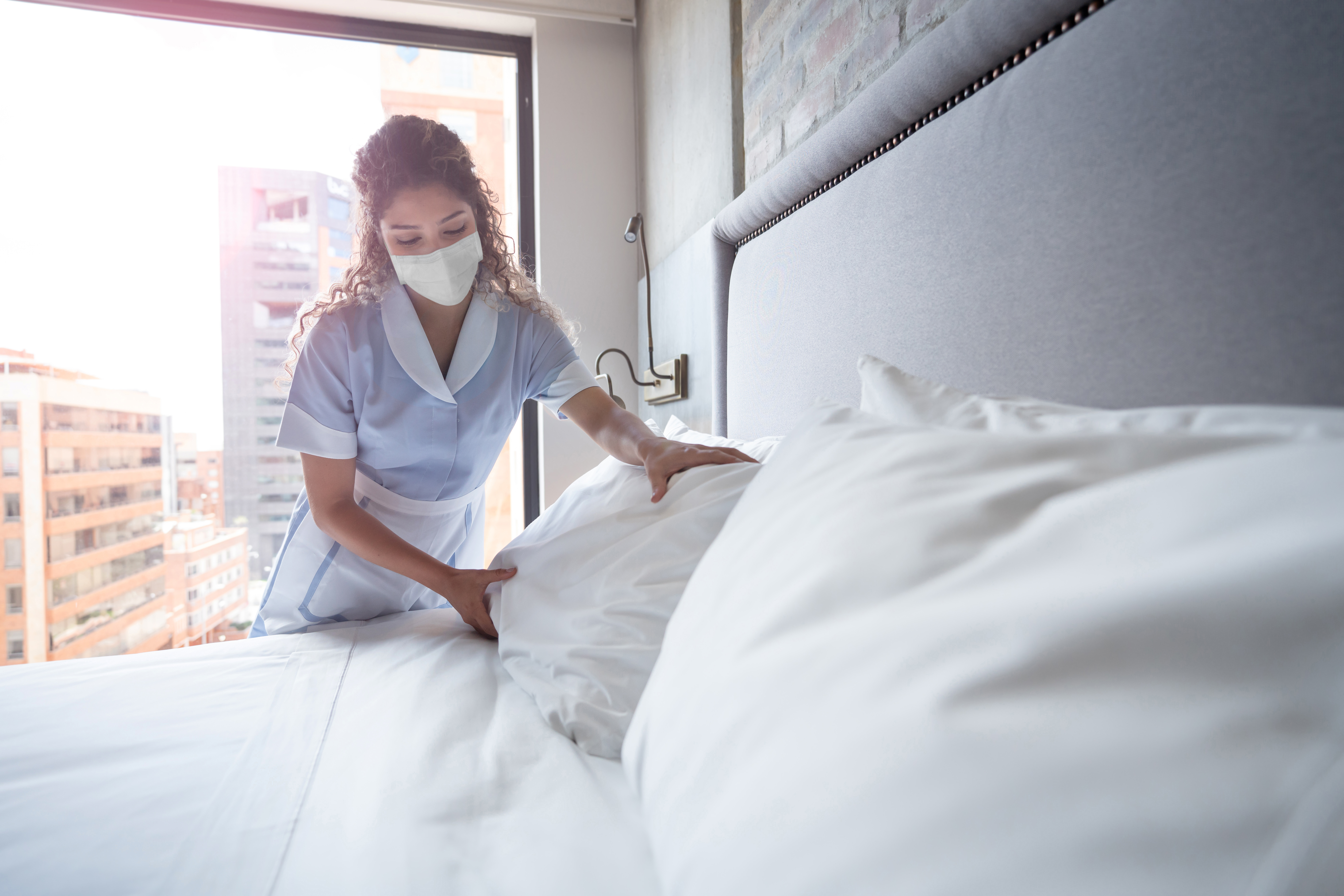 hotel housekeeper making a bed wearing a facemask