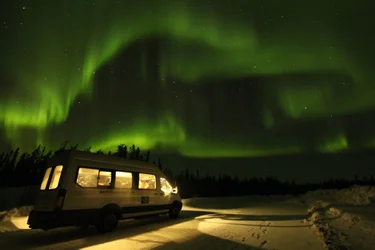 A white van is parked under the aurora borealis